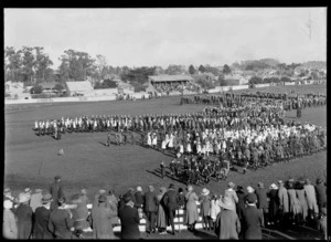 Ceremony at a park, with schoolchildren assembled in centre and spectators at perimetre and in grandstand, [reception for the Prince of Wales?], Whanganui