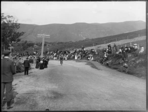 Motorcycle race, a motorcyclist riding up a hill, and spectators on the side lines, [Christchurch area?]