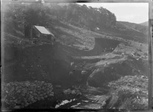 Otira Gorge, Westland District, featuring men digging and working on the entrance for the Otira Tunnel, with tent dwellings on the hillside