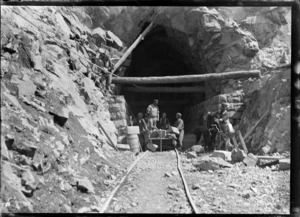Otira Tunnel, Westland District, with a man tending to a horse and men on a cart and working in the tunnel entranceway