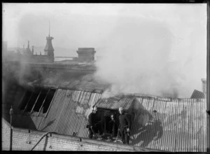 Firemen on the roof of a smouldering building, location unidentified