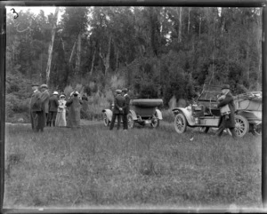 A group of people standing alongside their motor cars, location unidentified