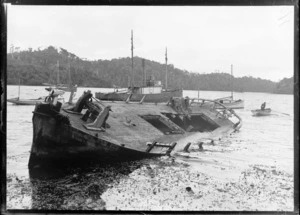 A wrecked ship in the harbour, with a man in a row boat and other boats moored in the harbour, location unidentified