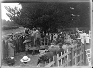 A group of people listening to a man giving a speech outside a Infectious Disease Hospital, probably Christchurch region