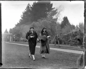 Horse racing, two women walking through the racecourse gardens, with a man walking in the background