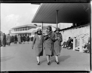 Horse racing, three women walking in front of the grandstand with their racing books