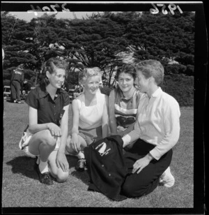 Three young women at an athletics meet at Hataitai Park, Wellington, with a young man holding a 1956 New Zealand Olympic Games Team blazer