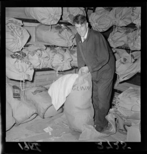 Edmund Hillary packs [bedding? clothing?] into a sack in preparation for the 1957 Commonwealth Trans-Antarctic Expedition, Department of Scientific and Industrial Research, Gracefield, Lower Hutt