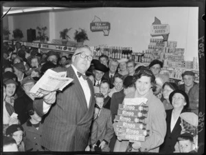 Celebrity, Selwyn Toogood, and an unidentified shopper with the give away prize of Rinso, at the opening of the Self Help store, Lambton Quay, Wellington