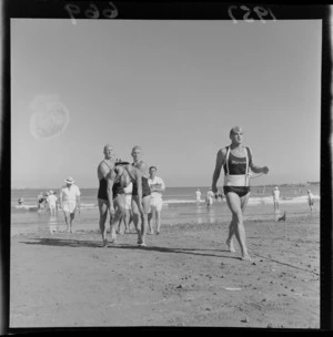 Surf lifesavers from Maranui Surf Life Saving Club are watched by officials as they perform a rescue at the 1957 National Surf Life Saving Championships, Lyall Bay, Wellington