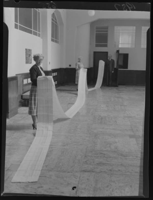 Two unidentified women and an unidentified man holding a length of paper recording the cash postings on the day's rates payments [Wellington City Council?]