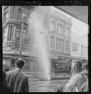 Burst water main on Willis Street, Wellington, in front of the office of the Evening Post newspaper, including tram tracks and businesses such as Martin's Shoe Store, Woodcraft Furniture, and Art Cabinet Company Limited