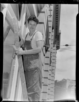 Barry Brown, boxer, standing on a ladder which is propped against the exterior of a building