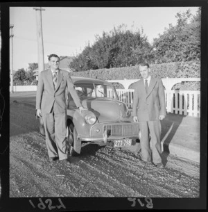 Two unidentified men stand in front of a Morris Minor on a metaled street in Levin