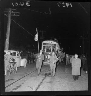 Farewell parade, final tram to Aro Street from Railway Station, Wellington, showing two unidentified man carrying a lamp and bagpipes and crowd watching