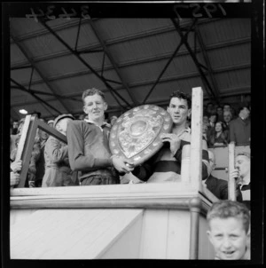 Wellington and Otago rugby captains holding the Ranfurly shield at Athletic Park, Wellington, including spectators watching