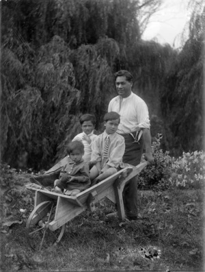 Man pushing a wooden wheelbarrow with three children sitting inside