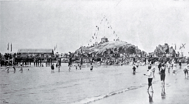 Children padding near the pier at Cave Rock, Sumner beach, decorated for a summer carnival, Christchurch