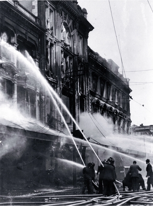 Firemen dampening down the main entrance of Ballantyne's, Colombo Street, Christchurch