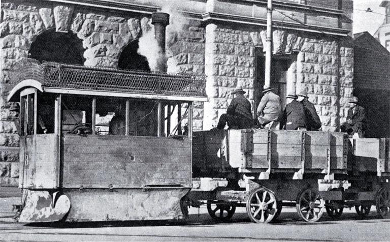 A Kitson steam tram runs past the Government Buildings in Cathedral Square with tramways workers on board