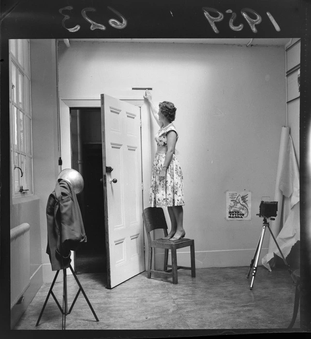 A woman standing on a chair to demonstrate the 'height cleared by a negro high jumper 7ft 1 1/4'