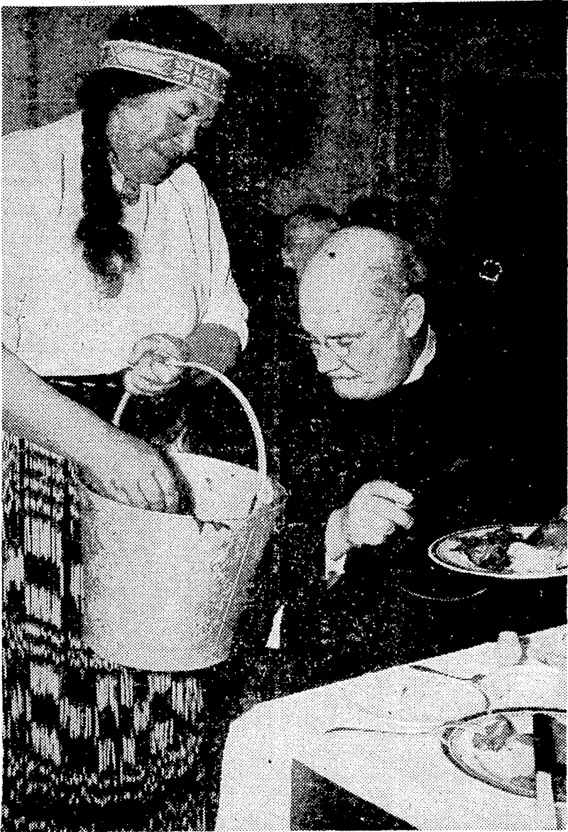 v ■ '"Sydney Morning Herald" Photo. Pork and vegetables cooked in Maori fashion being served to Canon Hammond by Mrs. H. W. Wehi at Hammondville, N.S.W., last week when the Maori choir was in Sydney. Members of the Maori choir ■ prepared and cooked all the food in the open air. (Evening Post, 06 August 1938)