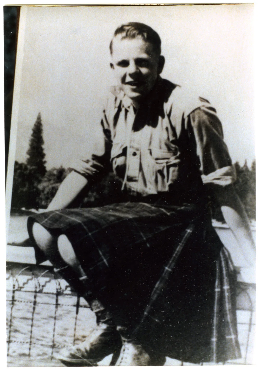 Unidentified boy wearing a kilt, sits on a metal fence