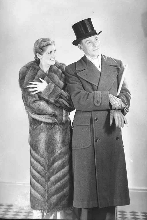 Full length portrait of male model wearing overcoat and top hat and female model wearing fur coat, for Dresswell Limited