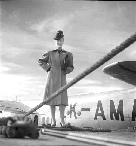 Showing Elaine Blythe in air hostess uniform, standing in front of Tasman Empire's flying boat 'Aotearoa' ZK AMA