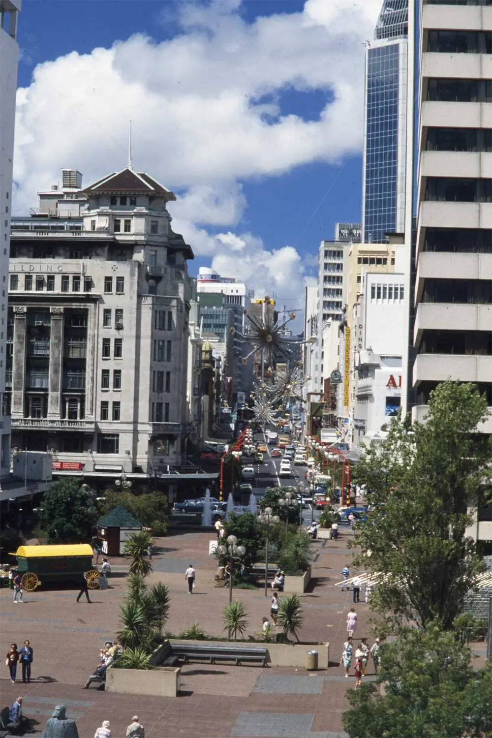 Looking south along Queen Street showing Queen Elisabeth Square (foreground), Customs Street (left to right across centre), the Dilworth building (left) and further along (on the right) the Country Wide Bank building, State Insurance, the Auckland Savings Bank, Government Life building, Dingwall building, Akai building, buses, pedestrians, christmas decorations