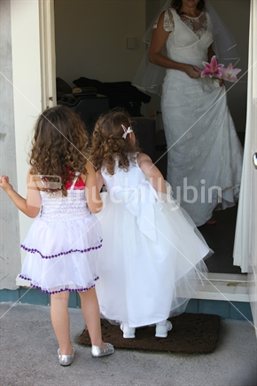Flower girls peek through the door at the bride as she prepares for her marriage