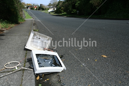 The remains of a computer screen smashed in a gutter in a suburban street