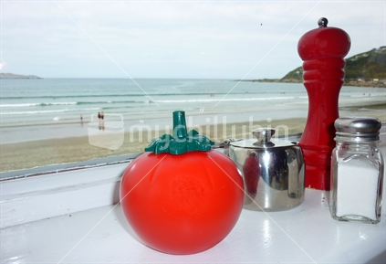 Retro tomato sauce bottle, pepper grinder, salt shaker and sugar bowl, overlooking a New Zealand beach.