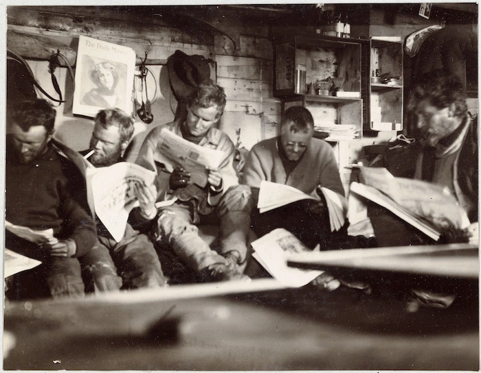 Men reading newspapers during the British Antarctic Expedition (1907-1909)