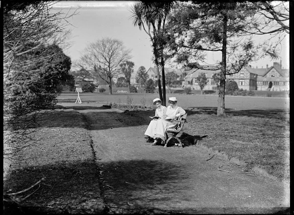 Two women in nurses' uniforms seated on a park bench