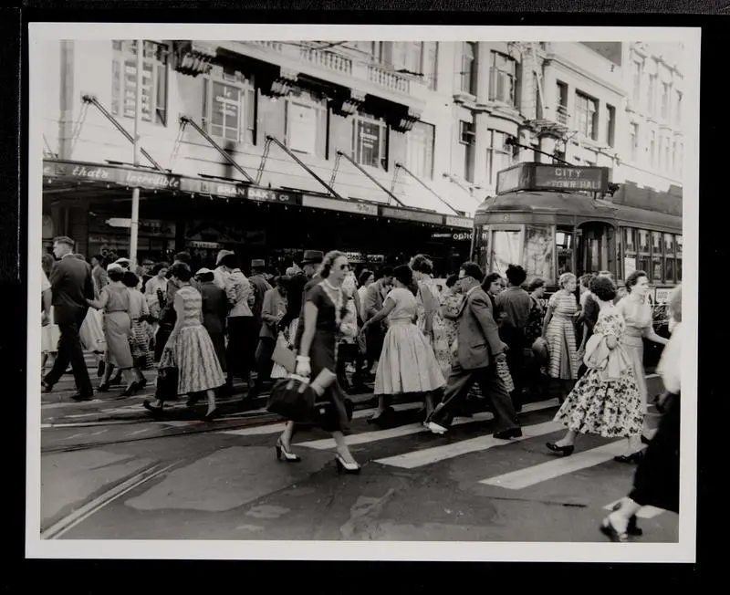 Crowds of pedestrians crossing Queen Street with tram waiting at crossing
