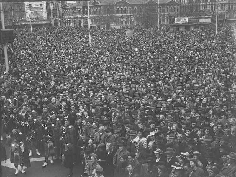 Celebrations. Crowd at WWII, Victory over Europe ( VE ) Day Celebration. Held 9 May 1945, With Flags and Pipers. Cathedral Square, Christchurch, Canterbury, New Zealand.