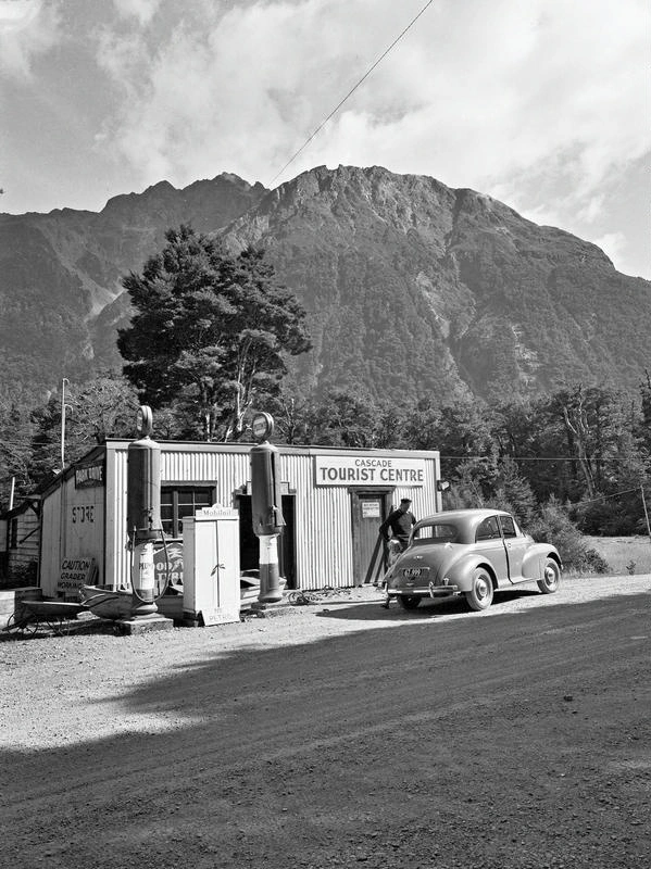 Service Station. Cascade Tourist Centre, Plume Petrol, Man Filling Morris Minor, Advertising on the Side for Park Drive Tobacco. Near Mt Aspiring. Otago, New Zealand.