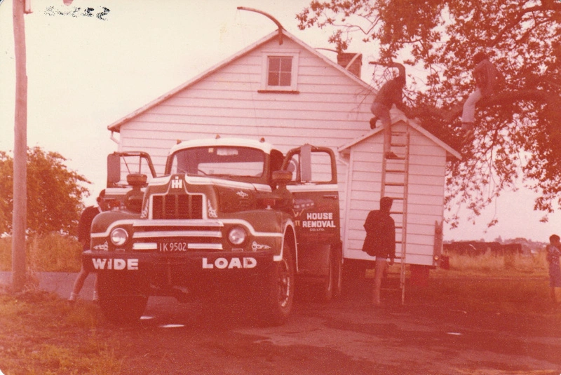 McDermott's Cottage on a transporter at Howick Historical Village jammed between an oak tree and a power pole. Warwick Johnson and David Mirams are about to prune the tree.