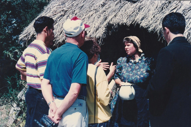 Debbie Benson in costume as Maggie Thompson talking to visitors in front of the sod cottage on a Live Day at HHV.
