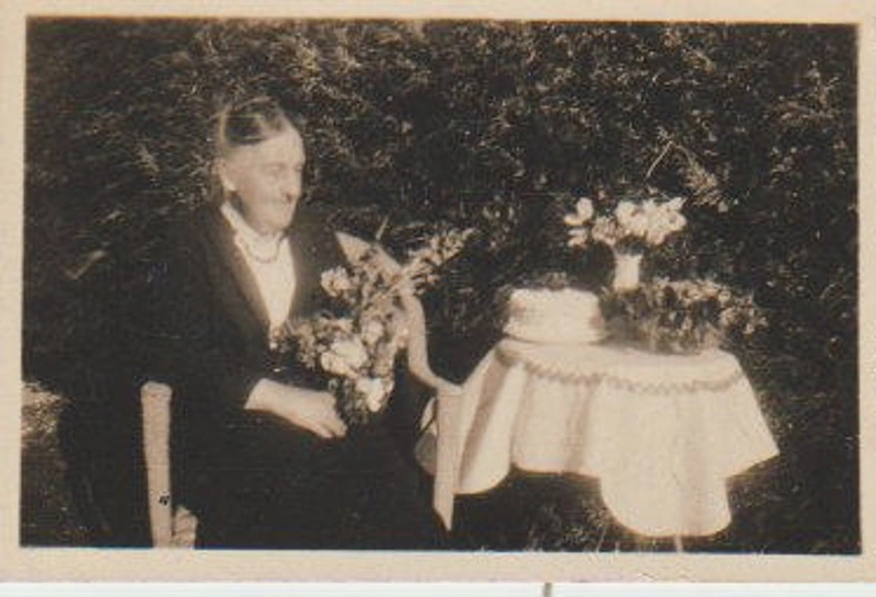 An elderly lady with flowers and a birthday cake
