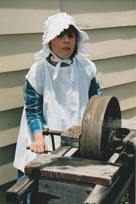 A little girl in costume using the grindstone in Howick Historical Village.