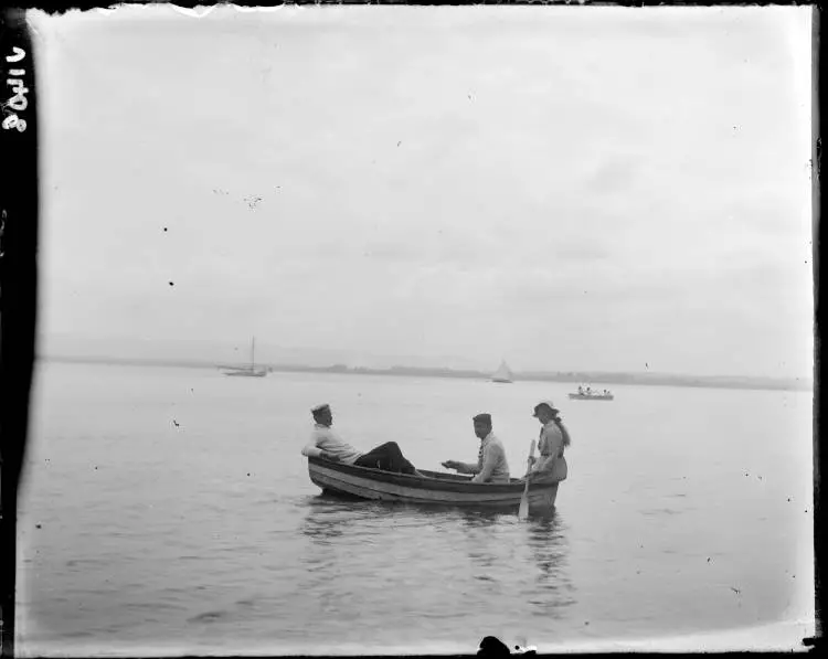 Three people in a dinghy at Kendall Bay, 1910