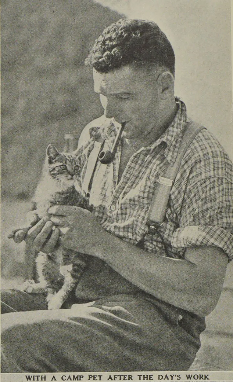 A man holds a cat while smoking his pipe after a day's work at the Aniseed camp near Kaikoura