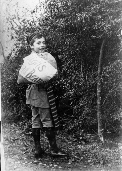 A boy dressed in an apron, holding a sack with the word "beans" over his shoulder