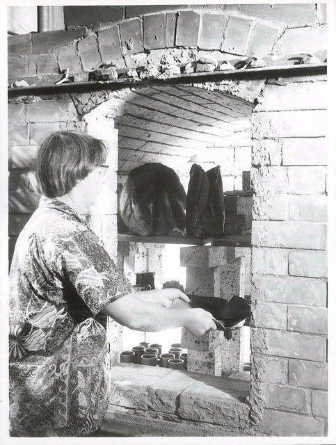 Mrs. Helen Mason taking some pottery from her kiln, which is fired using diesel oil. Mrs. Mason and four friends built the kiln themselves (possibly in Waitakere, Auckland)