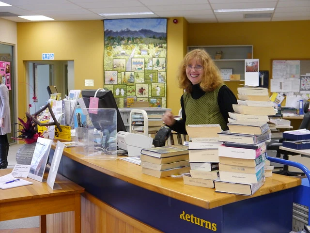 Library staff member with lots of books to return