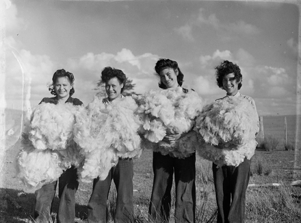 [Four women in paddock holding piles of sheared wool]