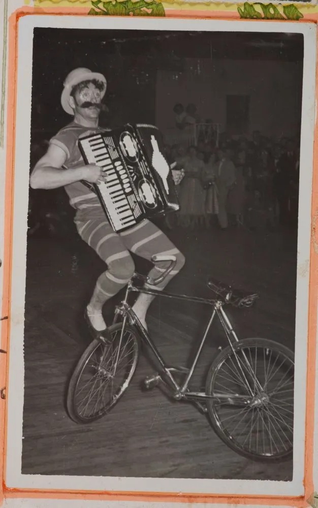 [Clown riding a bicycle and playing an accordion]