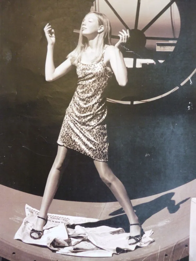 Sepia toned image of a female model standing on pages of a newspaper in an industrial setting